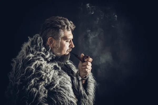 Twardy brodaty mężczyzna w futrzanym płaszczu palący fajkę — Zdjęcie stockowe