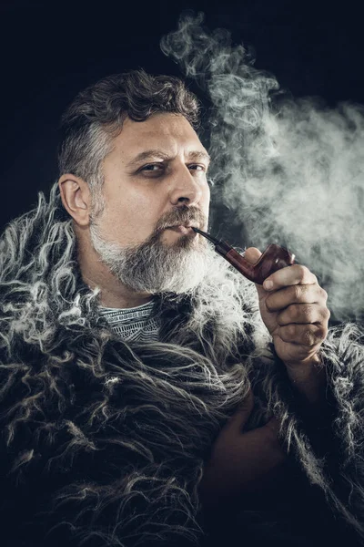 Vollbärtiger Mann im Pelzmantel, der Pfeife raucht — Stockfoto