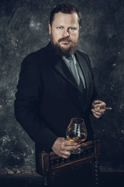 Hombre barbudo de confianza sólida en traje con vaso de whisky y un cigarro — Foto de Stock