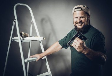 Yeşil tişörtlü neşeli sakallı zanaatkar zımba tabancasıyla eğleniyor.