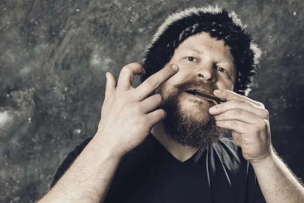 Matured man in fur hat playing jews harp Stock Picture