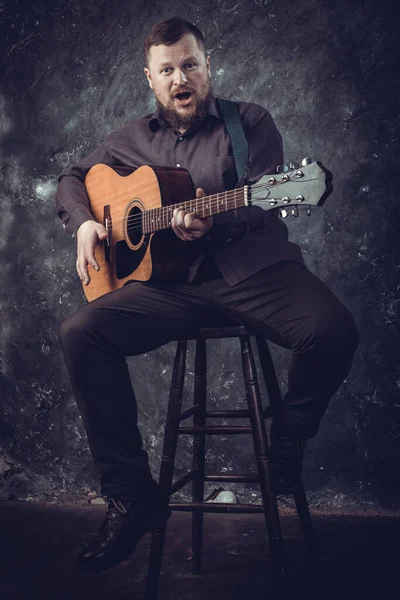 Mature musician plays acoustic guitar emotional studio portrait. — Stock Photo, Image