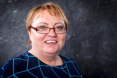 Mavi elbiseli orta yaşlı kadın gülümsüyor.