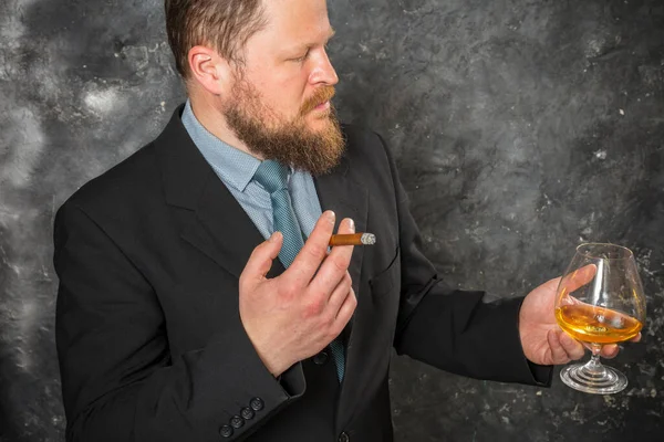 Stevige zelfverzekerde man met baard in pak met glas whisky en sigaar — Stockfoto