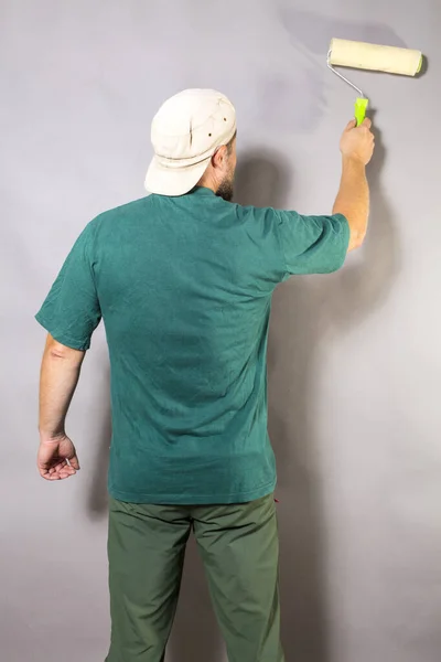 Fröhlicher bärtiger Polier im grünen T-Shirt mit Pinselwalzenblick von hinten — Stockfoto