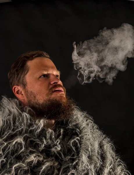 Hombre de barba sólida vestido con un manto de piel exhalando vapor — Foto de Stock