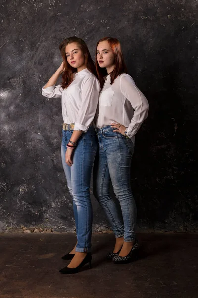 Beautiful teen girls dressed in white shirt and blue jeans standing close to each other — Stock Photo, Image