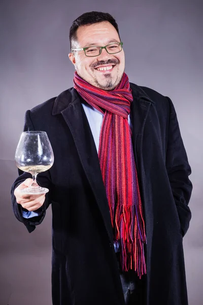 Solido uomo allegro in cappotto e fazzoletto in piedi con vetro di vino — Foto Stock