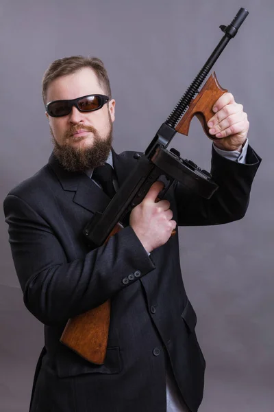 Dojrzały mężczyzna w okularach przeciwsłonecznych ubrany w garnitur z pistoletem Tommy — Zdjęcie stockowe