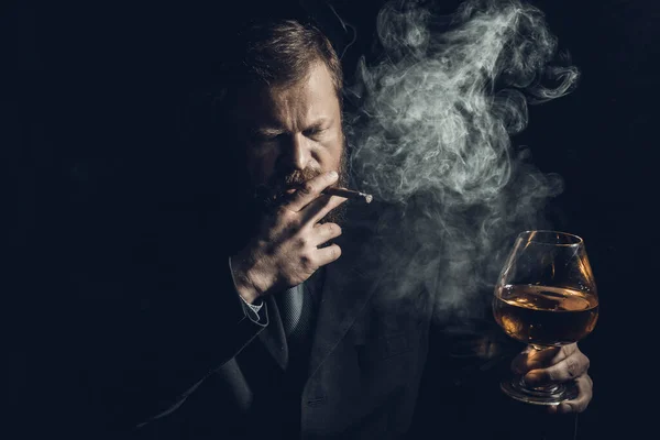 Stevige zelfverzekerde man met baard in pak met glas whisky en sigaar met rook — Stockfoto