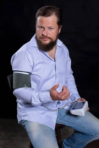 Зайнятий бородатий чоловік з тонометром вимірювання тиску на себе — стокове фото