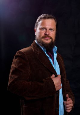 Siyah arka planda takım elbise giymiş şık sakallı bir adam..