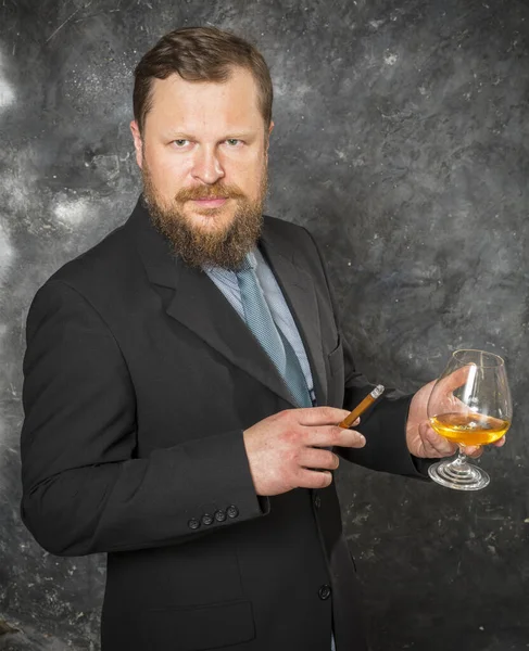 Hombre barbudo sólido y confiado en traje con vaso de whisky y cigarro — Foto de Stock