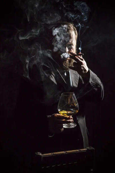 Hombre barbudo sólido y confiado en traje con vaso de whisky y cigarro — Foto de Stock