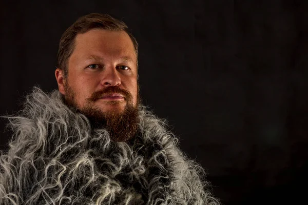 Solid bearded man in a fur mantle studio portrait