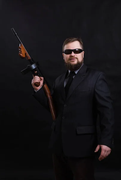 Dojrzały brodaty mężczyzna w okularach przeciwsłonecznych ubrany w garnitur z pistoletem Tommy 'ego — Zdjęcie stockowe