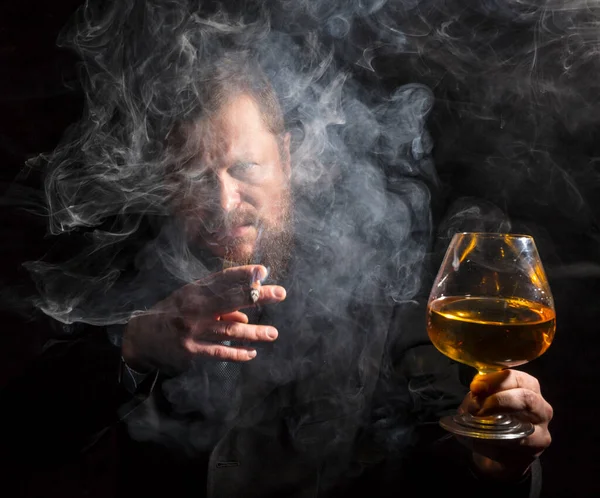 Solide homme barbu confiant en costume avec verre de whisky et cigare avec fumée — Photo