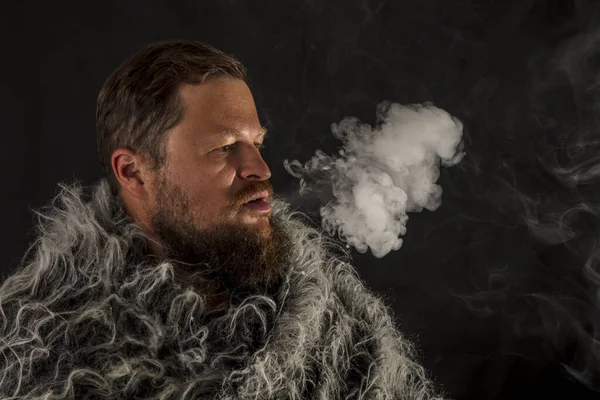 Hombre de barba sólida vestido con un manto de piel exhalando vapor — Foto de Stock