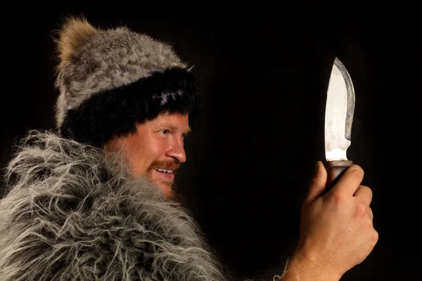 Bearded hunter dressed in a fur mantle and fur hat with knife Royalty Free Stock Images