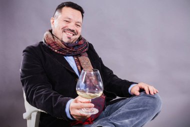 Eşarplı neşeli adam bir kadeh şarapla oturuyor.
