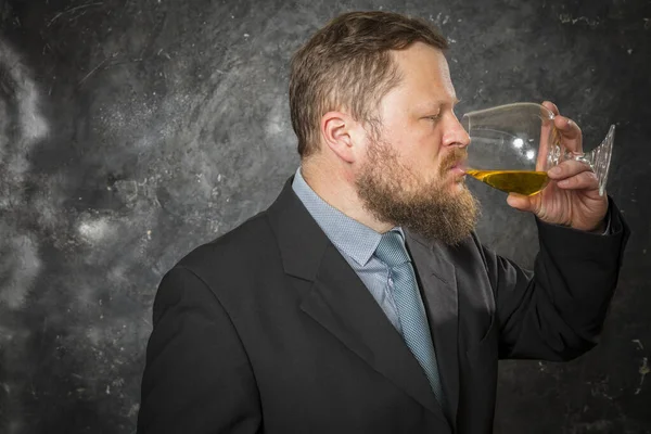 Vaste bebaarde man in pak proeft whisky in een glas — Stockfoto