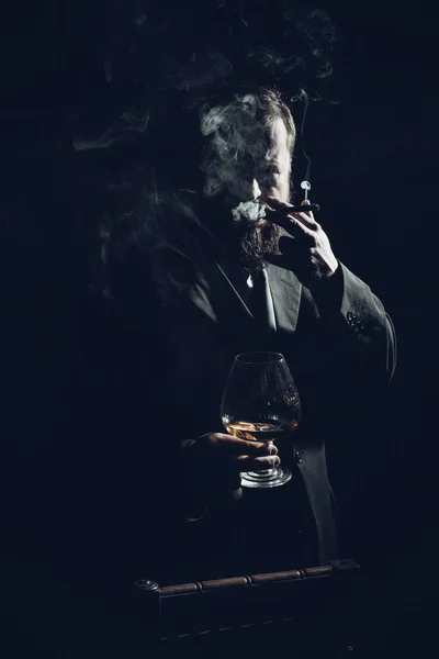 Stevige zelfverzekerde man met baard in pak met glas whisky en sigaar — Stockfoto
