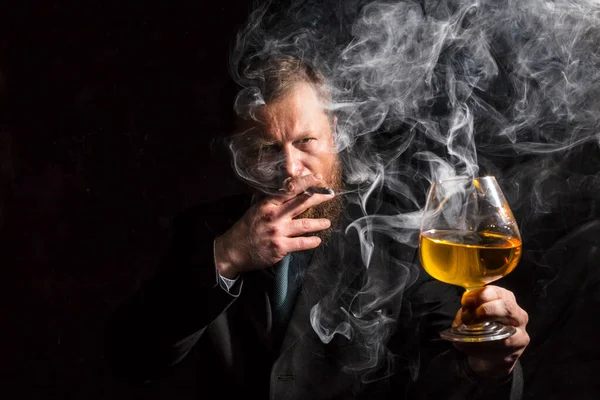 Solide homme barbu confiant en costume avec verre de whisky et cigare avec fumée — Photo