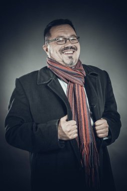 Gözlüklü, ceketli ve mendilli, neşeli bir adam.