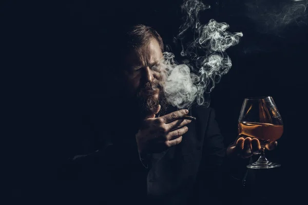 Hombre barbudo sólido y confiado en traje con vaso de whisky y cigarro con humo —  Fotos de Stock