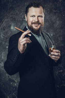 Bir bardak viski ve puroyla takım elbiseli, kendinden emin, sakallı bir adam.