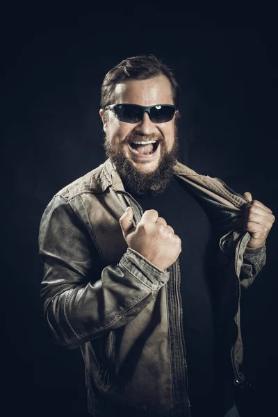 Emocjonalny brodaty mężczyzna w okularach przeciwsłonecznych ubrany w skórzaną kurtkę z radością wygrywa — Zdjęcie stockowe