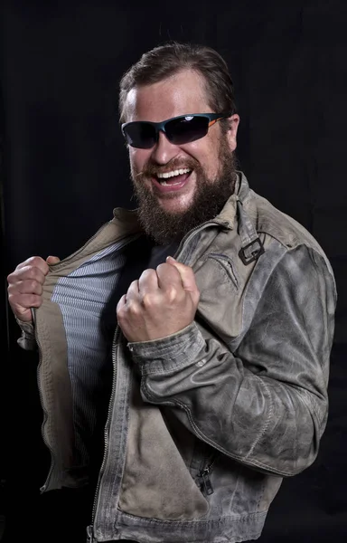 Homem barbudo emocional em óculos de sol vestido com jaqueta de couro está feliz em ganhar — Fotografia de Stock
