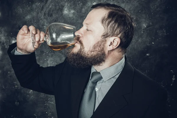 Fast skäggig man i kostym provsmakning whisky i ett glas — Stockfoto