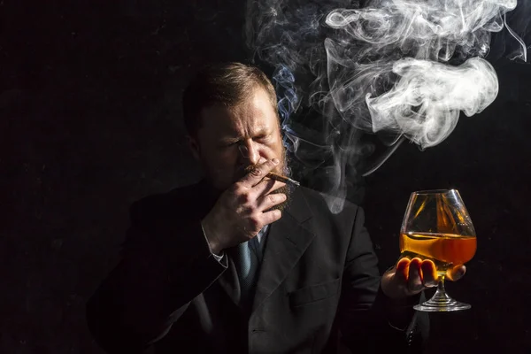 Solide homme barbu confiant en costume avec verre de whisky et cigare avec fumée — Photo