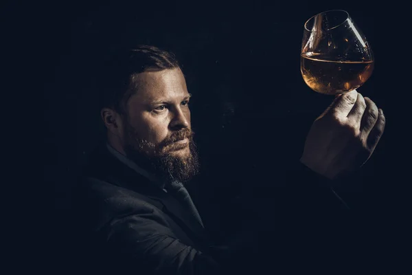 Szilárd, magabiztos szakállas férfi öltönyben egy pohár whiskyvel. Jogdíjmentes Stock Képek