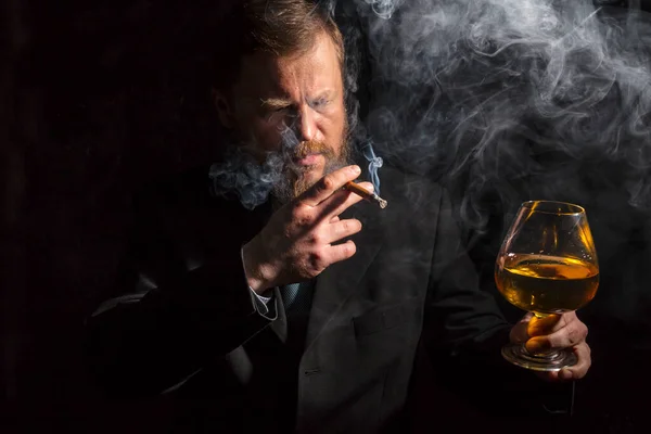 Stevige zelfverzekerde man met baard in pak met glas whisky en sigaar met rook — Stockfoto