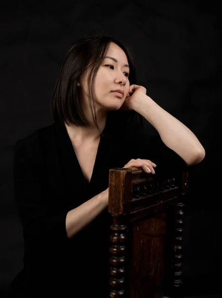 Hermosa mujer coreana vestida con vestido negro sentada en silla estudio retrato. Imagen De Stock