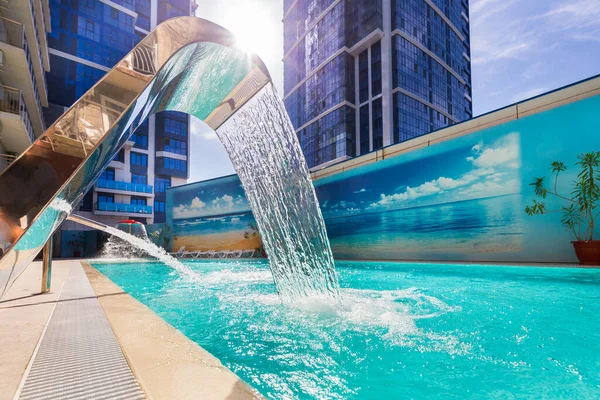 Piscine extérieure avec cascade sur fond de paysage urbain. — Photo