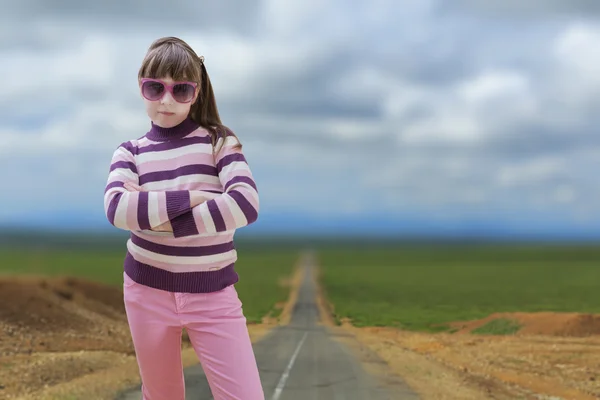 Tienermeisje in roze draagt zonnebril met weg op achtergrond — Stockfoto