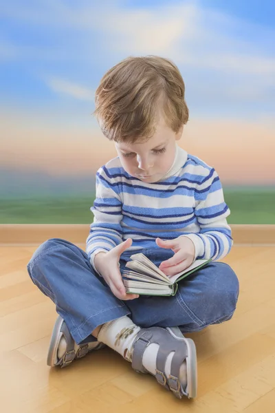 Pojke läser boka sittplatser på golvet med sunrise bakgrund — Stockfoto