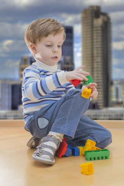 Menino brincando com a construção de plástico com edifícios contemporâneos no fundo — Fotografia de Stock