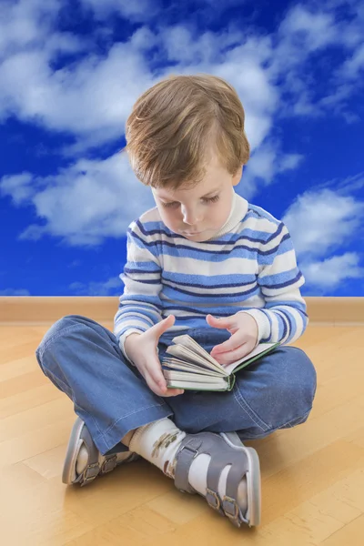 Jongen lezen boek zitplaatsen op de verdieping met wolk hemel op achtergrond — Stockfoto