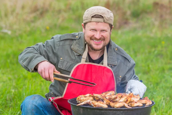 Чоловік готує барбекю на газоні шеф-кухар посміхається — стокове фото