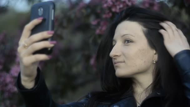 Молодая девушка, красивая, брюнетка делает селфи со смартфоном улыбается — стоковое видео