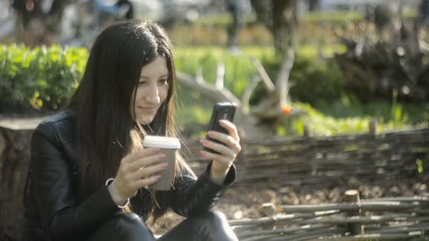 Eine junge schöne Frau, die Kaffee trinkt und ihr Smartphone benutzt — Stockvideo