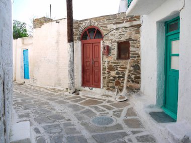 Taş kaldırım yolundaki beyaz duvarda mavi kırmızı renkli kapılar.