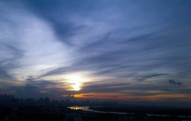 Akşam Günbatımı Şafağı Yağmurlu bir günde Yüksek gökdelenli şehir manzarası ve nehir hattı, bulutlu ve kasvetli gökyüzü pastel renkli