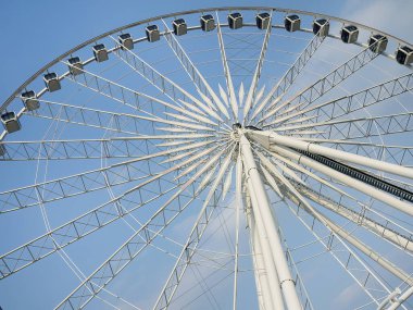 Lunapark eğlencesi konsepti. Solucan bakışı büyük bir gözlem çarkına bakıyor. Beyaz çelik yapı, teller ve yolcu gondolları var. Güneşli bir günde eğlenceli bir yolculuğun soyut geometrik ayrıntıları.