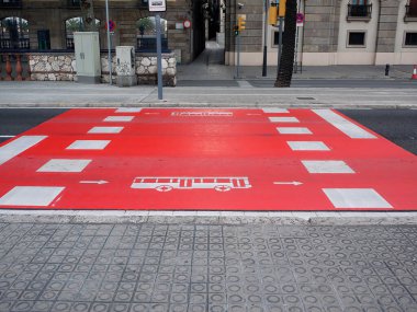Toplu taşıma altyapısı kavramı. Beyaz otobüs sembolü ve özel bir öncelik şeridini gösteren oklarla dolu parlak kırmızı bir yol yüzeyi. Kentsel bir bölgedeki desenli bir kaldırımdan görünüm.
