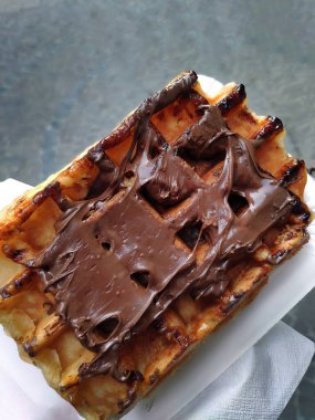 Tek kullanımlık kağıt tabakta servis edilen taze pişmiş Belçika waffle 'ının ağız sulandırıcı görüntüsü. Bu popüler sokak yemekleri zengin eritilmiş çikolatalarla kaplıdır, hızlı atıştırmalıklar ya da kahvaltı düşkünlüğü için mükemmeldir..